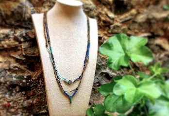 Collana con piccoli elementi blu esposta su busto chiaro all'aperto